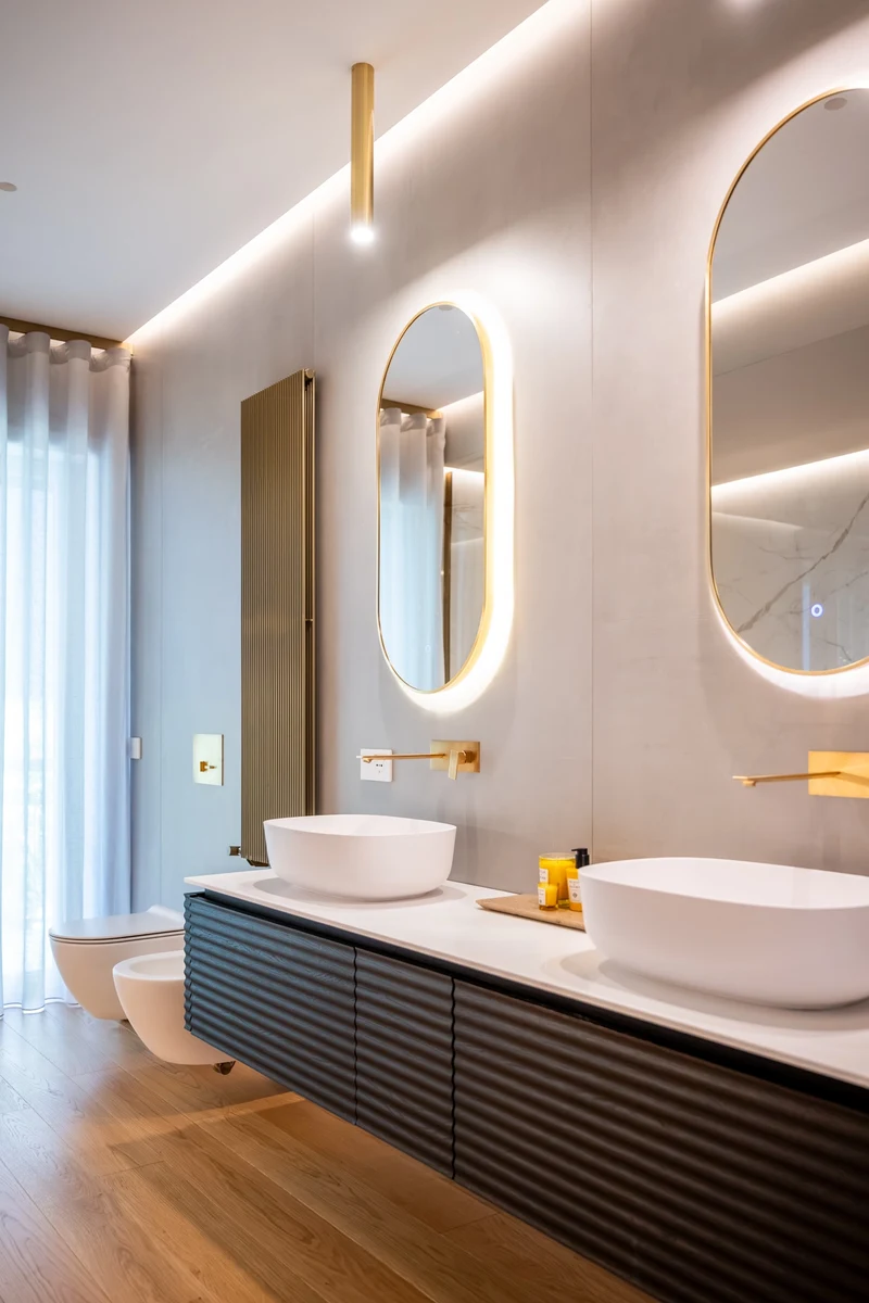 Focus bagno con doppio lavello, specchi ovali retroilluminati, rubinetteria oro e parquet