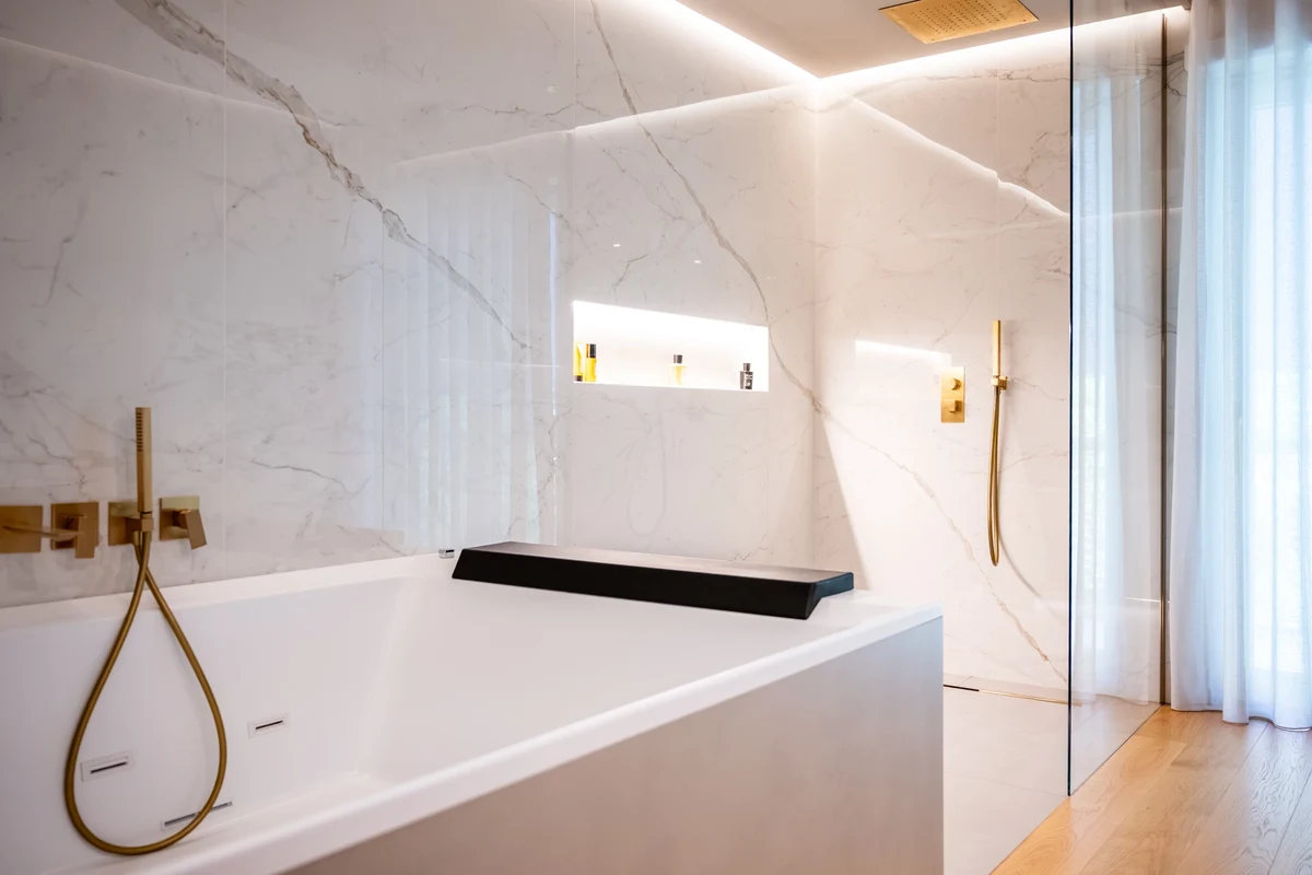 Prospettiva vasca e doccia walk in con nicchia illluminata, rivestimenti in marmo e rubinetteria oro