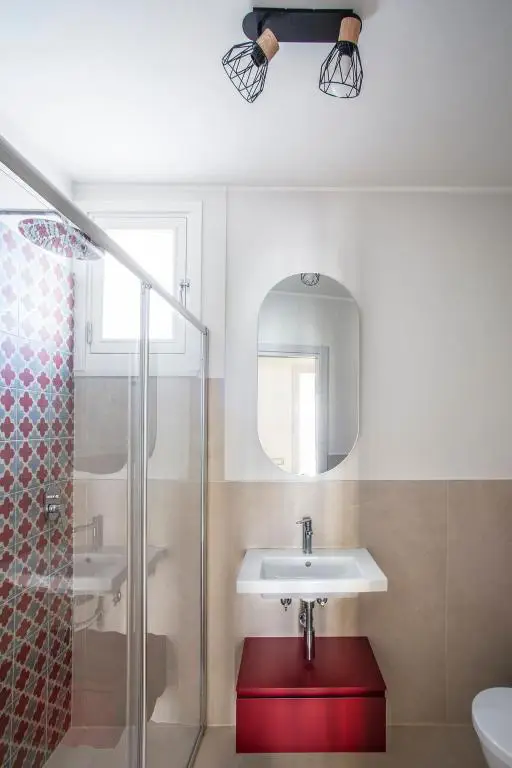 Bagno con parete doccia con piastrelle con maioliche, lavandino sospeso e specchio ovale