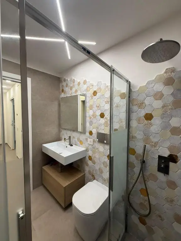 Bagno con parete rivestita di piastrelle esagonali, lavello sospeso e mobile in legno