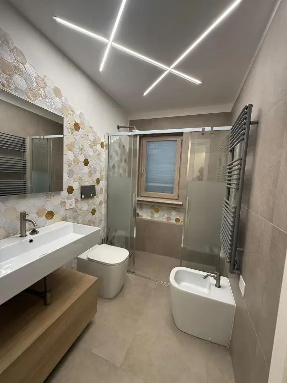 Bagno con sanitari a terra filomuro, rivestimenti parete con piastrelle esagonali e termoarredo grigio