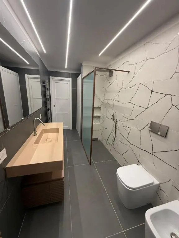 Bagno con lavello sospeso effetto materico, doccia walk in con rubinetteria e profili in oro