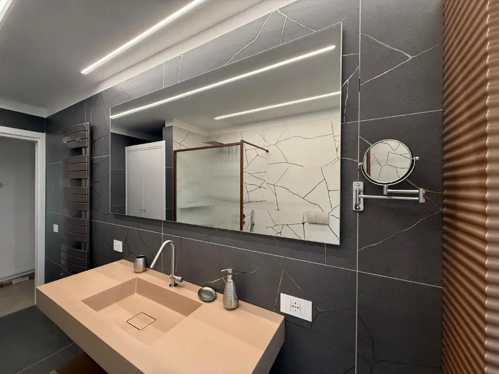 Parete bagno con rivestimenti scuri, lavello sospeso beige, specchio rettangolare e termoarredo grigio scuro
