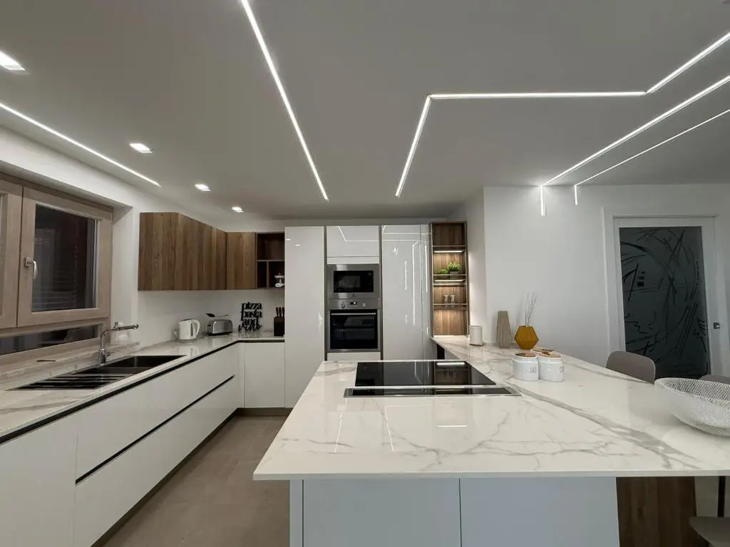 Cucina con isola centrale in marmo bianco, ante bianche e luci a led sul soffitto