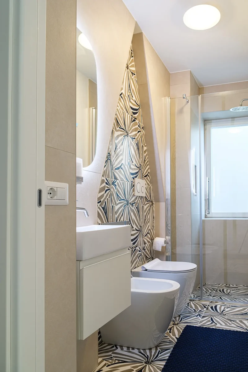 Visuale bagno con mobile bianco, specchio ovale retroilluminato e parete decorata con rivestimenti ornamentali