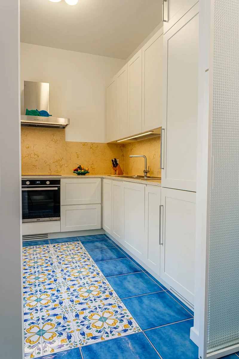 Cucina angolare bianca con pavimento con piastrelle azzurre e decorate con maioliche