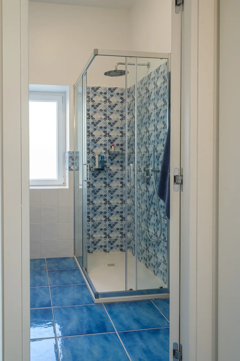 Dettaglio bagno con doccia con parete rivestita da piastrelle decorate con maioliche azzurre