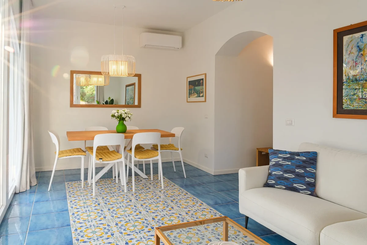 Visuale sala con tavolo in legno, sedie bianche e divano chiaro