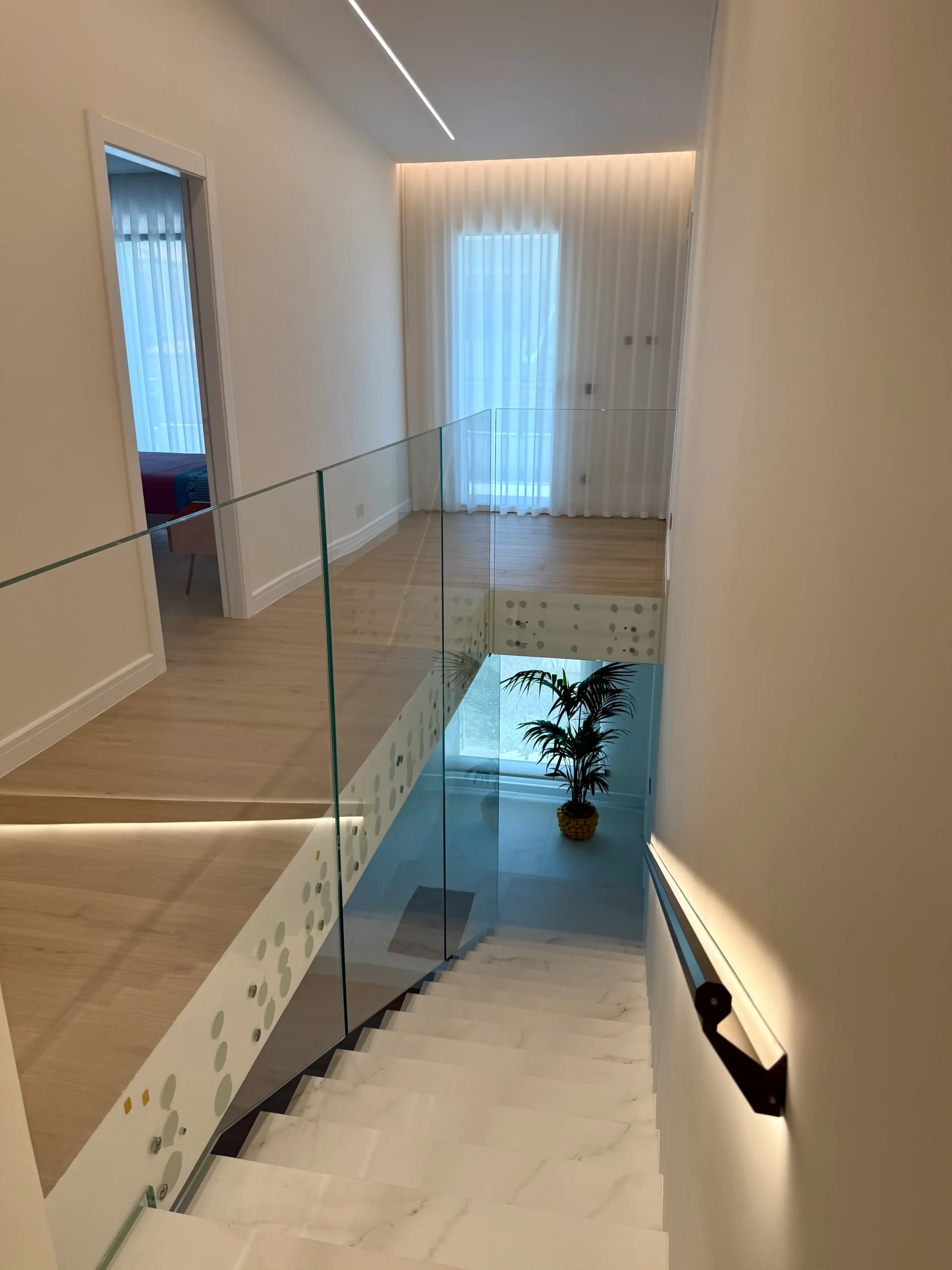 Visuale di scale bianche in marmo, parapetto in vetro e corridoio con parquet