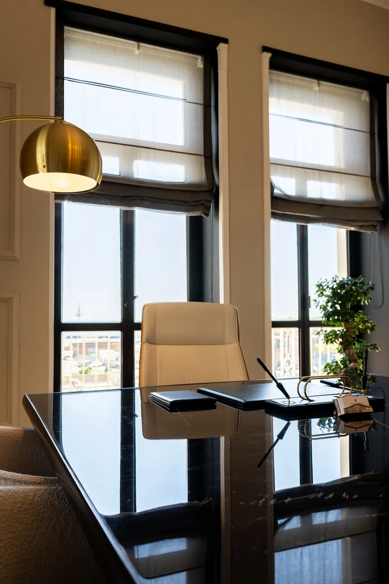 Prospettiva di uno studio professionale in cui si vede tavolo da riunione, sedie in pelle, lampada a soffitto color oro e finestre